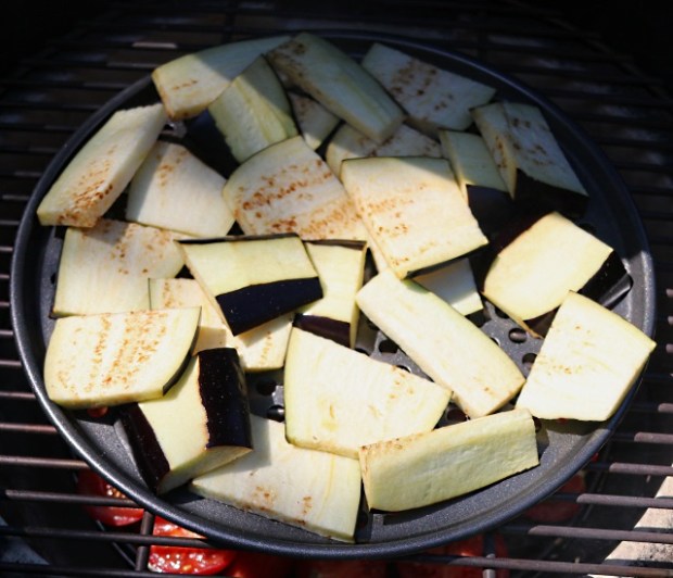 Aubergines smoking on a pizza baking pan with holes in the base