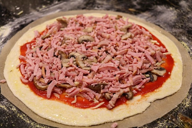Pizza dough on parchment paper with topppings ready to bake