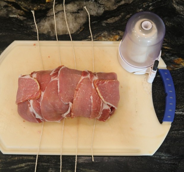 Lengths of string underneath the pork log ready to hog-tie it