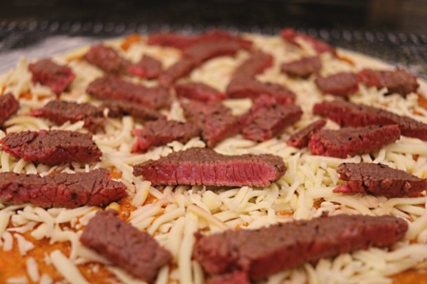Strips of flash-fried steak on the pizza prior to cooking