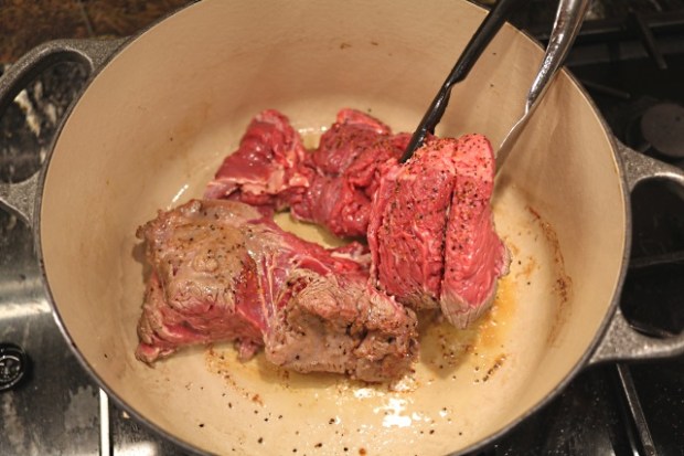 Turning the braising steak with kitchen tongs