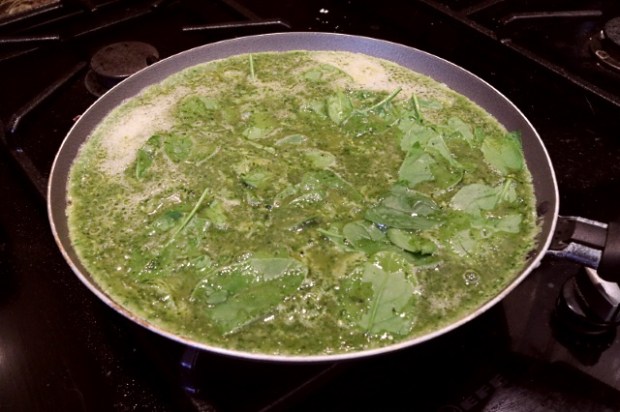 Green egg omelette with spinach leaves cooking on a stove